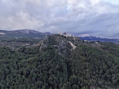 Uçsuz bucaksız gökyüzünün ve alçak bulutların altında, engebeli kireçtaşı çıkıntısı ve kalınlığında ağaçlık bir tepe.