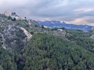 Yeşil çam ormanlarına tepeden bakan harabeler ve su deposu, teraslı yamaçlar, Akdeniz çalıları, sessiz