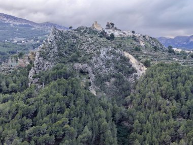 aerial scene isolated rocky summit with moody low clouds hugging ridge, stark contrast between pale stone