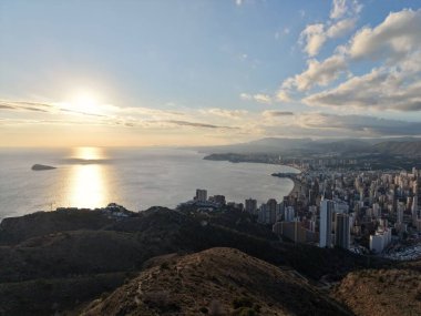 Ufuk çizgisi olan gün batımı, yükselen binalar kuyruk, suyun altın yansıması, dramatik