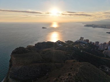 Okyanus ve şehre tepeden bakan gün batımı, önplandaki kayalık patika yürüyüş perspektifi, sıcak