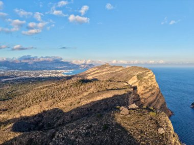 Gök mavisi denize bakan gökyüzü tepesi, uzun gölgeli yürüyüşçü bakış açısı