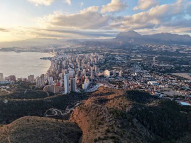 Mimari ufuk çizgisi engebeli tepeler ve körfez tarafından yumuşak akşam ışığında çerçevelenmiş, fotoğrafçı bakış açısı