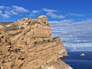 derin denizin üzerindeki engebeli kumtaşı uçurumu, parlak mavi gökyüzünün altında ufuk yakınındaki küçük feribot, katmanlı kaya tabakası