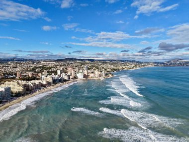 Sabahları dalgalarla yükselen kıyı şeridi. Göbek binalarıyla kaplı kumlu sahil üzerinde insansız hava aracı perspektifi.,