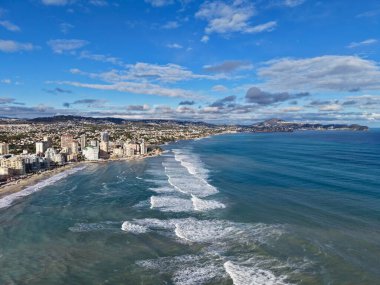 Kara kara düşünen bulutların altında dramatik sahil kenti, güçlü dalgalar beyaz köpükle kıyıya çarpıyor, dalgalı
