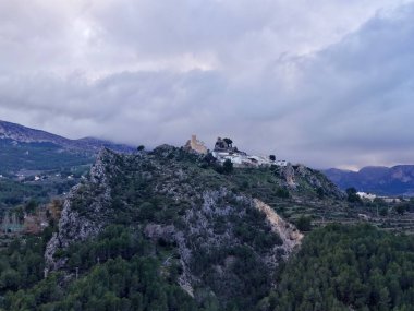 Yoğun çam ormanlarına ve dolambaçlı yollara bakan kayalık tepedeki beyaz şapel.