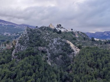 Beyaz harabeye ve panoramik gözcülüğe giden kayalık tepe yolu yoğun çam ve engebeli arazide dolambaçlı yol.