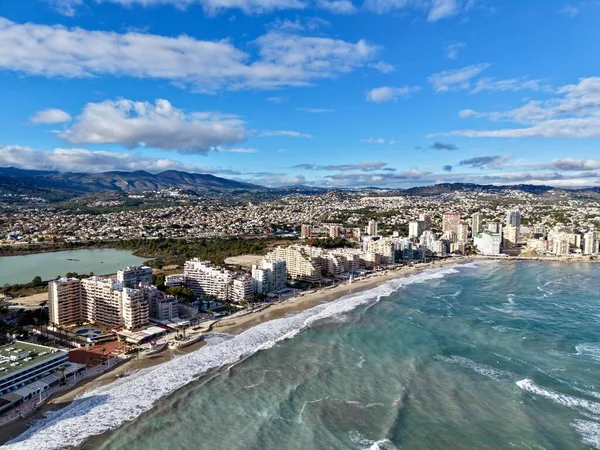 Havada dalgalanan mavi gökyüzü, kumlu sahil kenti, marina boyunca uzanan kuleler.