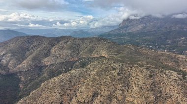Çalı ve kayalık tepelerin üzerindeki kurak hava sırtı, jeolojik araştırma perspektifi, kahverengi yamaçlardaki bulut gölgeleri