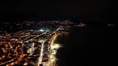 Gece hava sahasının ışıkları kıyı şeridini izliyor, sakin karanlık deniz, aydınlık gezinti güvertesi, dağınık arabalar.,