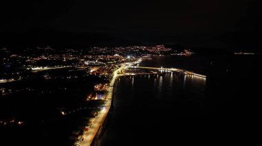 Gece körfezi kıvrımlı ışıklar sahil şeridine sarılıyor, sakin su aynaları kehribar yansımaları, marina siluetleri,