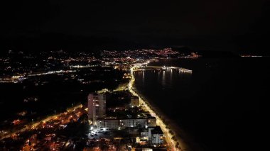 Kehribar ışıklarıyla parlayan gece marinası ve sahil şeridi, yüksek ve kıyı yolu, yansımalar.