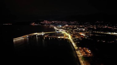 Gece hava rıhtımı karanlığa doğru parlıyor, kıyı yolu aralıksız ışıklarla aydınlatılıyor, tekne siluetleri, sükunet