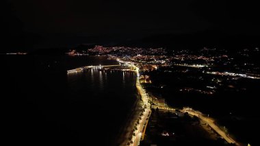 Parlayan kıyı şeridine sahip gece hava limanı döngüsü, sakin yansıtıcı su, sürekli sokak lambası şeridi,