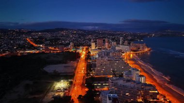 Alacakaranlık Sahil Kenti Bulvarı sokak lambalarıyla aydınlatılıyor, şafaktan önce mavi gökyüzü, sahil boyunca turuncu yol şeridi,