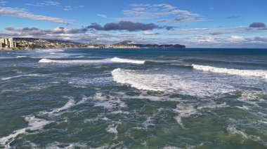 İnsansız hava aracı kıyı şeridini, dalgaları ve desenli denizi, uzak sahillerdeki güneşli kasabayı, geniş manzarayı gözler önüne seriyor.