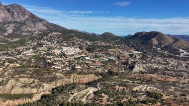 Güneşli vadi şehri hava manzarası kümelenmiş çatılar, virajlı yollar, tarlalar ve yumuşak tepeleri gösteriyor.