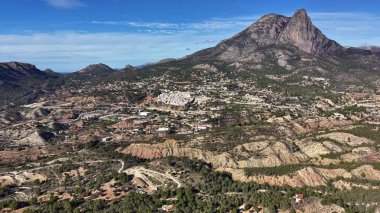 Dağ zirvesi, kayalık zirveyi, kurak yamaçları ve açık mavi gökyüzünün altındaki dağlık köyü gösteriyor.
