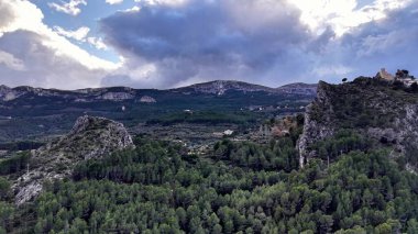 Fırtınalı bulutların altındaki ormanlık vadi harabelerle kayalık, dramatik ışık, gök gürültülü gökyüzü, dağcı
