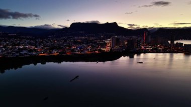 Gece şehir ışıkları sakin limana yansıyor ufuktaki siluetli dağlara, aydınlık kulelere