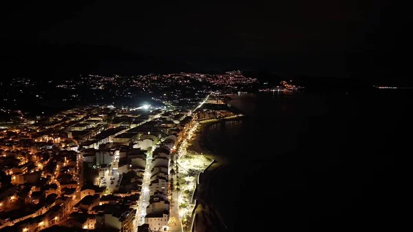 Gece hava sahasının ışıkları kıyı şeridini izliyor, sakin karanlık deniz, aydınlık gezinti güvertesi, dağınık arabalar.,