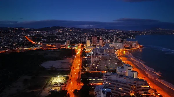 Alacakaranlık Sahil Kenti Bulvarı sokak lambalarıyla aydınlatılıyor, şafaktan önce mavi gökyüzü, sahil boyunca turuncu yol şeridi,