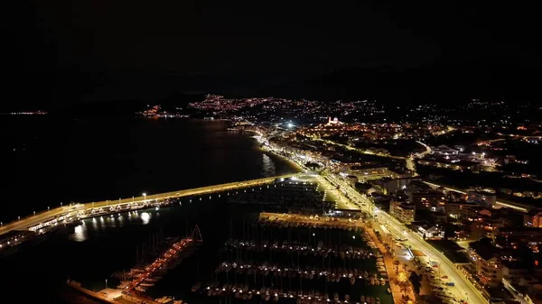 Liman ışıkları sahil limanı marinasını ve köprüyü süpürüyor. Altın parıltı ve deniz manzaralı yollarla aydınlatıyor.