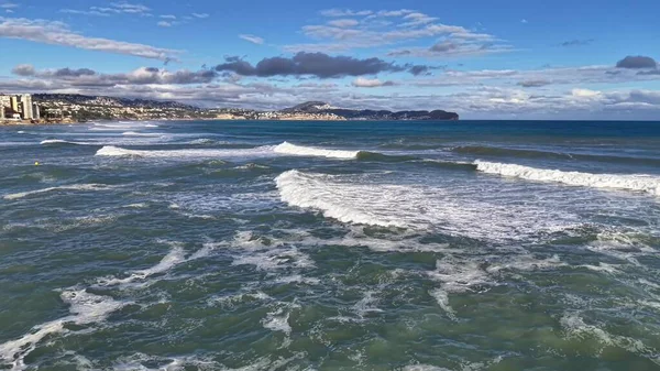 İnsansız hava aracı kıyı şeridini, dalgaları ve desenli denizi, uzak sahillerdeki güneşli kasabayı, geniş manzarayı gözler önüne seriyor.