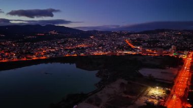 Hava alacakaranlık göl kenti ışıkları parlayan sakin su aynası, mavi alacakaranlık altındaki uzak tepeler, sessiz