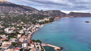 Körfezi olan kıyı köyü havası, turkuaz sığ sularda hafif dalgalar, kıyı şeridi beyaz.