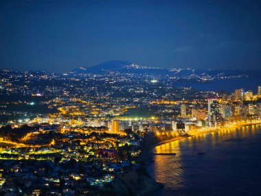 Gece ışıl ışıl yanan kıyı kenti, altın gezinti güvertesi ışıkları, suda dans eden yansımalar, yoğun.