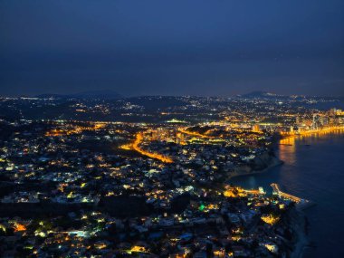 Alacakaranlıktaki kıvrımlı kıyı otoyolunun geniş hava manzarası. Durmaksızın ışık saçan bir şerit.
