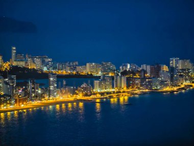 Derin gece gökyüzünün altında altın rıhtım yayı, kıyı şeridini şekillendiren sokak lambaları, modern