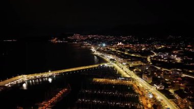 Liman ışıkları sahil limanı marinasını ve köprüyü süpürüyor. Altın parıltı ve deniz manzaralı yollarla aydınlatıyor.