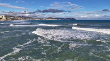 İnsansız hava aracı kıyı şeridini, dalgaları ve desenli denizi, uzak sahillerdeki güneşli kasabayı, geniş manzarayı gözler önüne seriyor.
