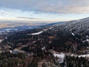 Expansive winter valley with winding river and distant town under luminous sky, frosted treeline and scattered