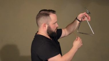 Siyah T-Shirt sakallı bir adam, Vurmalı Çalgı Üçgeni üzerinde oynuyor. Parlak Duvarlar Arka Plan üzerinde.