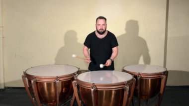 Siyah T-Shirt, vurmalı enstrüman Timpani oynayan bir sakallı bir adam. Parlak duvarlar arka plan üzerinde.