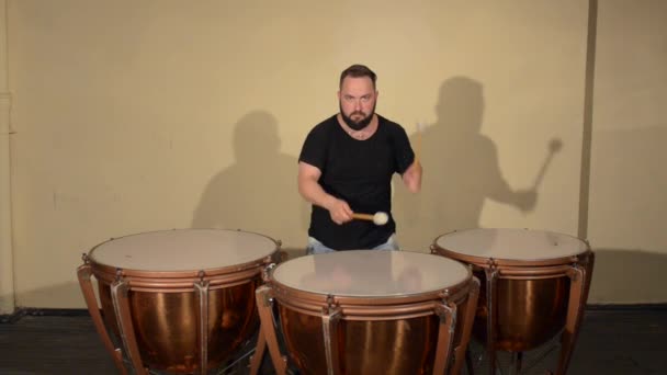 Een Man met een baard in zwart T-Shirt, spelen op de pauken van de percussie-Instrument. op de achtergrond van de heldere wanden. — Stockvideo