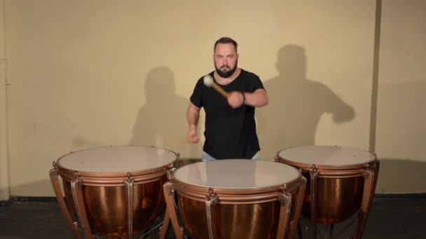 Um homem com uma barba em camiseta preta, tocando no instrumento de percussão Timpani. no fundo das paredes brilhantes . — Vídeo de Stock