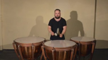 Siyah T-Shirt, vurmalı enstrüman Timpani oynayan bir sakallı bir adam. Parlak duvarlar arka plan üzerinde.