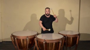 Siyah T-Shirt, vurmalı enstrüman Timpani oynayan bir sakallı bir adam. Parlak duvarlar arka plan üzerinde.