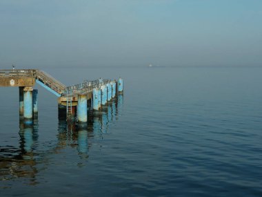İskele sütunları, sisli gökyüzünün altındaki Baltık Denizi sularına yansıdı. Kopyalama alanı