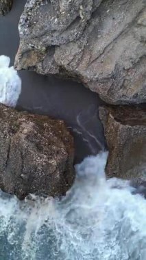 Kıyı şeridindeki kayalar ve uçurumlar arasında okyanustan gelen bir dalganın insansız hava aracı videosu..