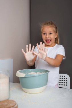 Mutlu kız evde pişirirken una bulanmış ellerini gösteriyor..