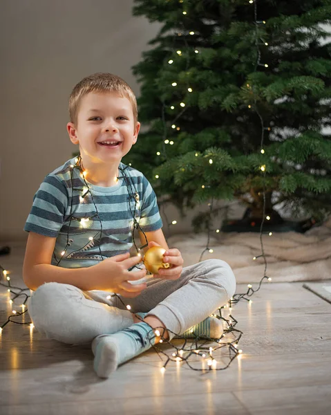 Mutlu bir çocuk Noel ağacını ışıklar ve süs ile süslüyor..