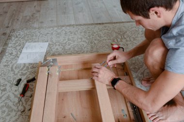 İnsan, aletleri ve talimatları kullanarak evde ahşap mobilya monte eder. Apartmanı geliştirmek için DIY projesi.