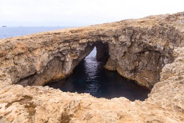 Doğal bir kireçtaşı oluşumu Malta 'da kayalık bir sahil şeridinde karanlık bir su havuzu üzerinde bir deniz kemeri oluşturur. Açık deniz ve uzak gemiler ufukta görünüyor..