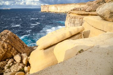 Malta adasında bulutlu bir gökyüzünün altında dalgalı, koyu mavi bir Akdeniz 'e bakan yüksek kireçtaşı uçurumlarının manzarası..